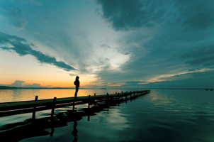 person standing on jetty at sunset